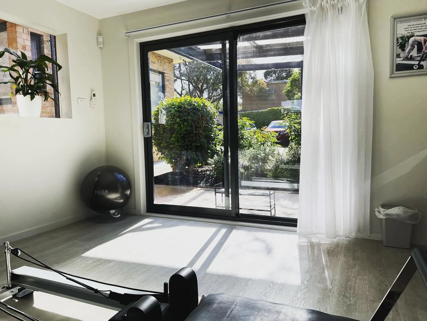 Sunlit reformer Pilates studio, reformer foreground, sliding door onto the garden